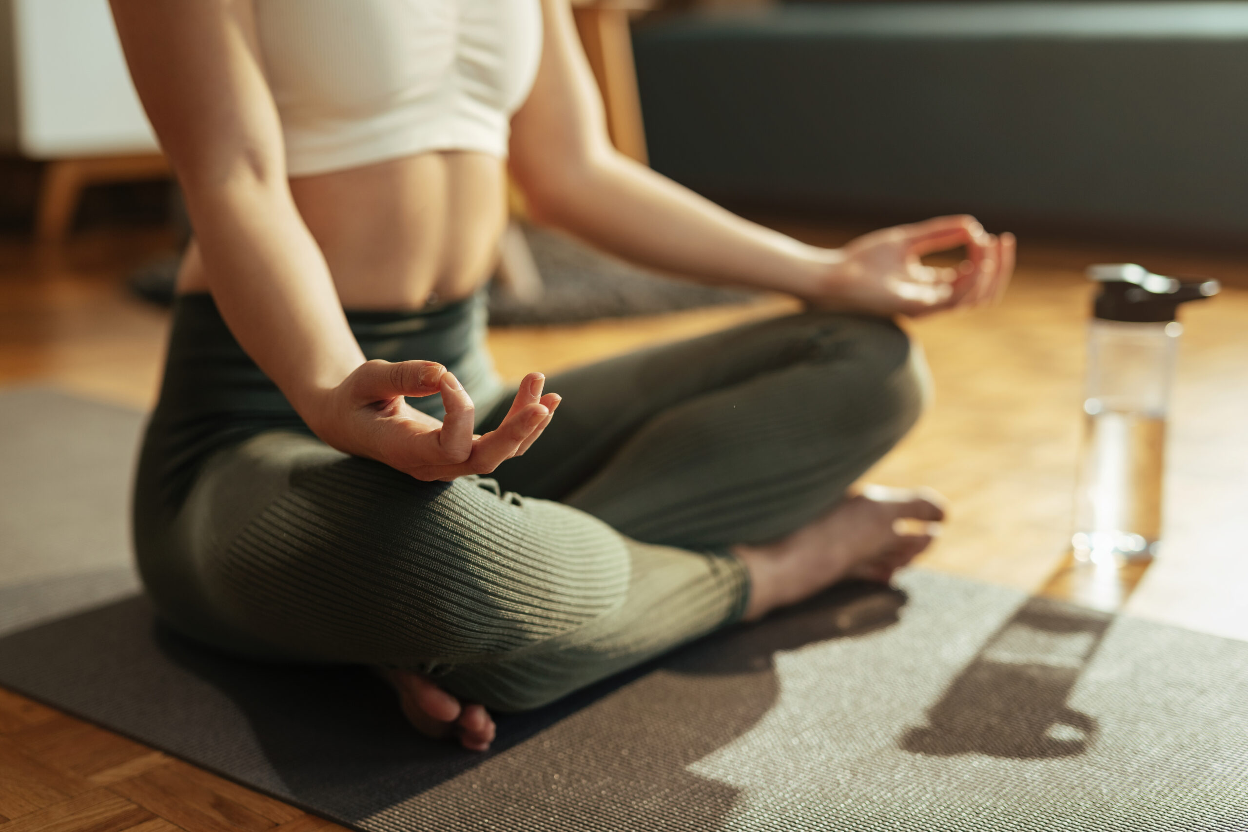 Close-up of woman meditating on lotus position at home.
